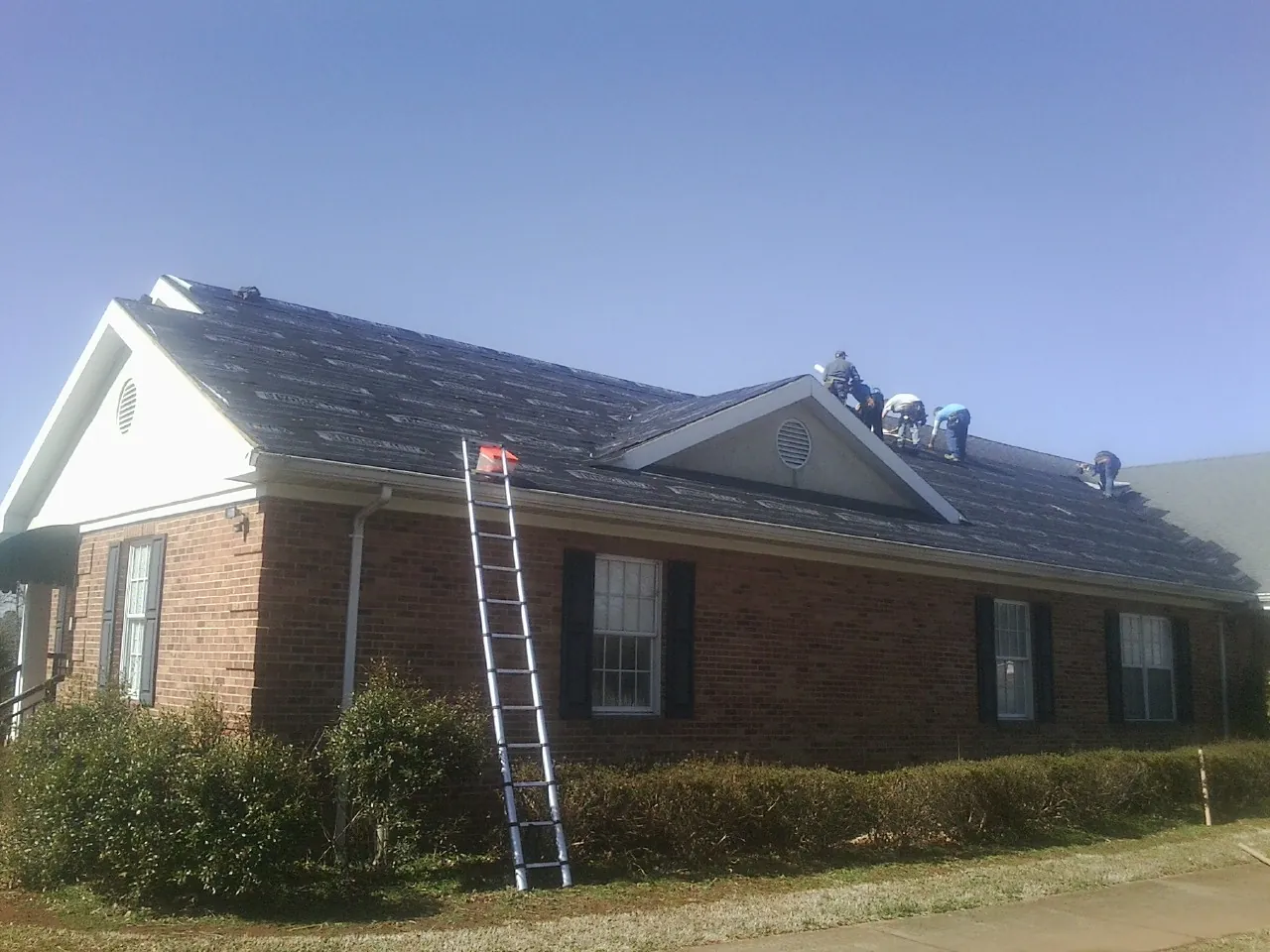 Crew tearing shingles off a brick ranch roof with a ladder set — Metal Roof Repair work by our crew in Neffs