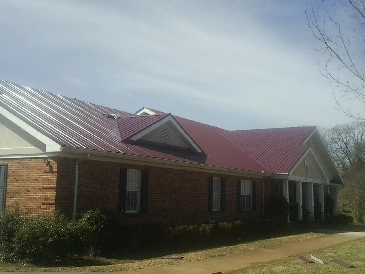 Red metal roof with gabled entries on a long brick building, from a Hail Damage Roof Repair job in Neffs