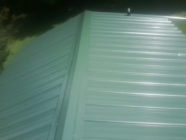 New green metal panels meeting at the ridge of a roof — Flat Roof Repair work by our crew in Neffs