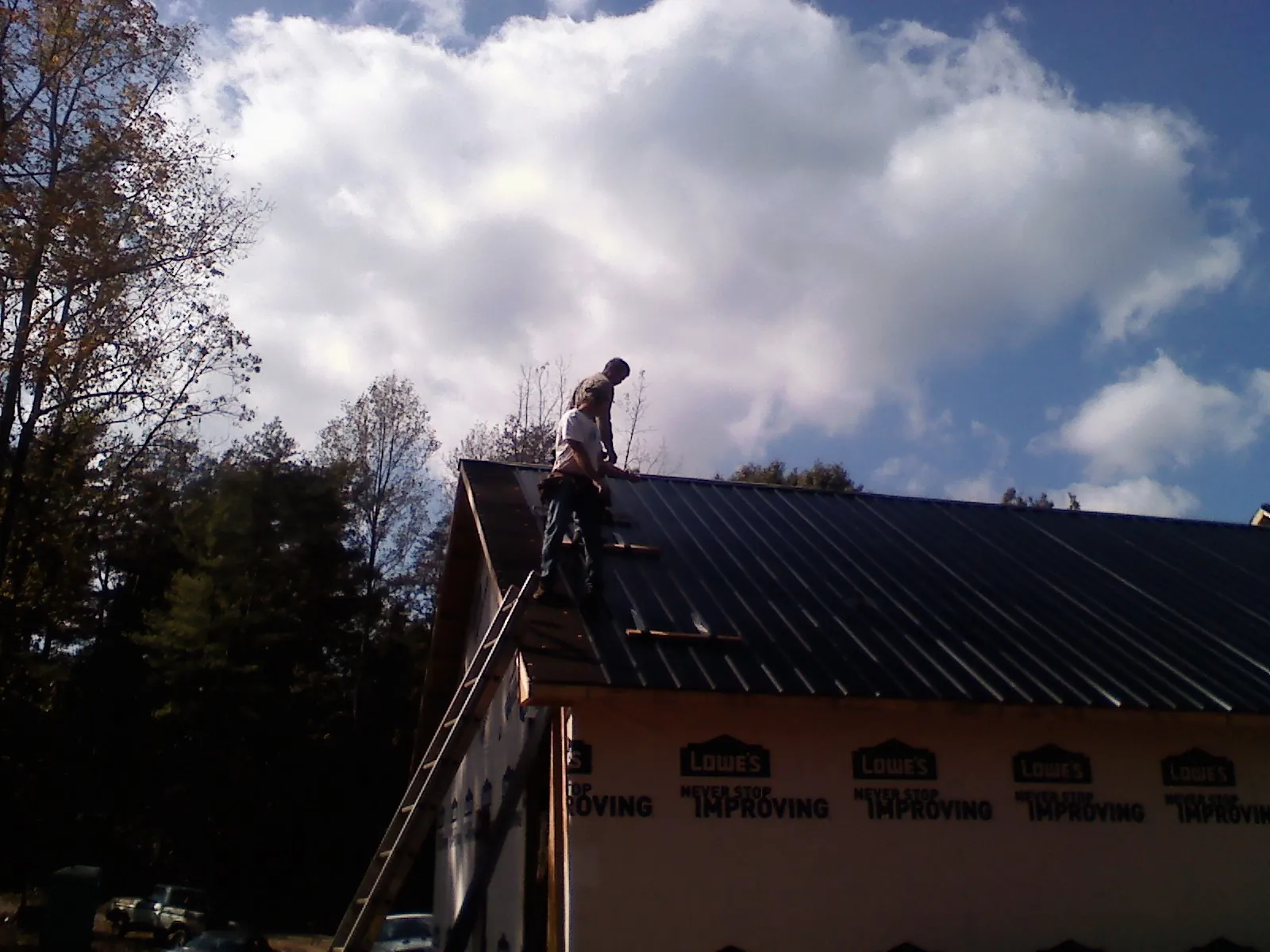 Roofer fastening dark metal panels high against a cloudy sky, from a Roof Inspection job in Neffs