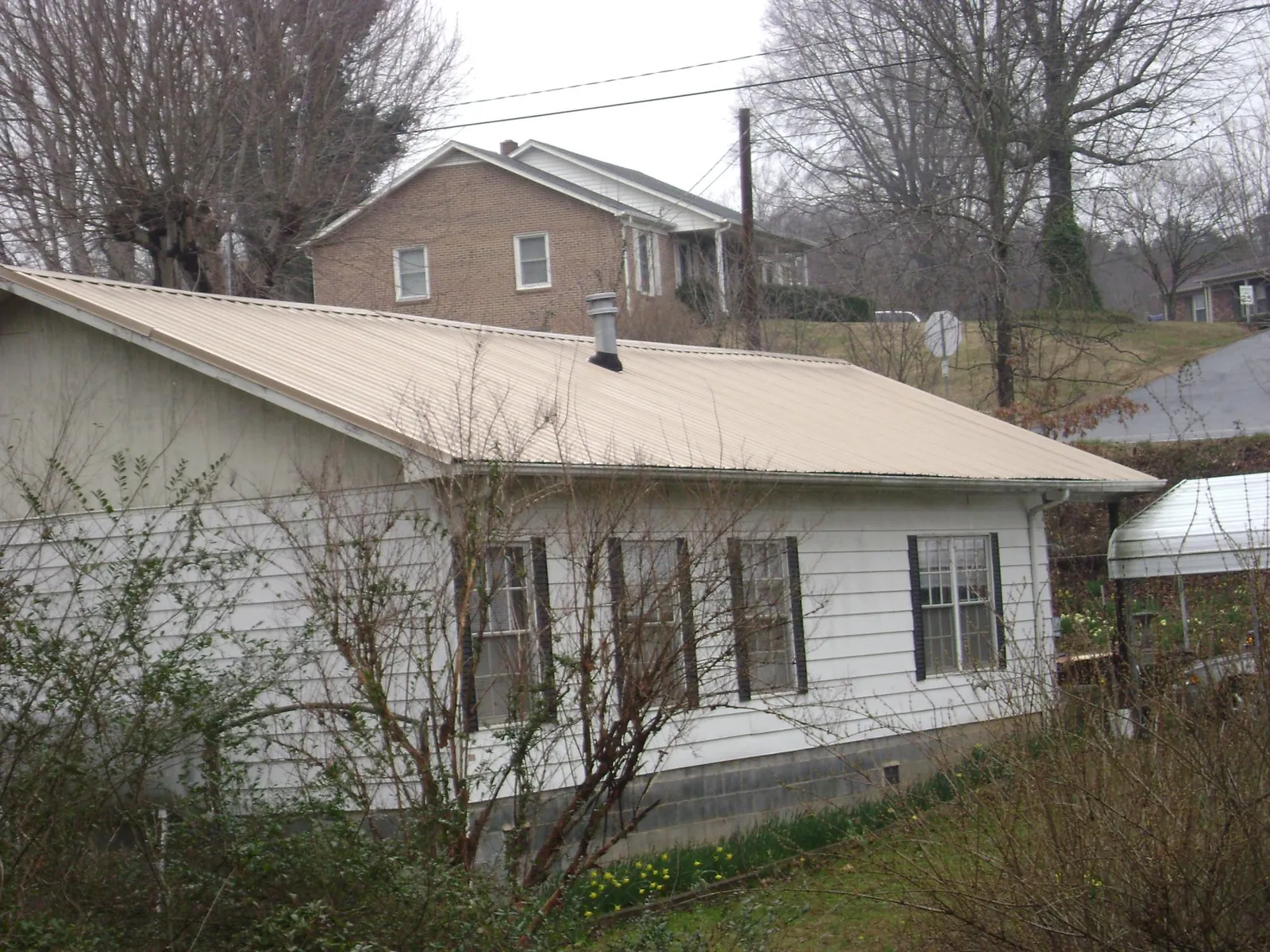 Tan metal roof on a white sided house set into a hillside — Commercial Roofing by Roofing Brothers in Neffs